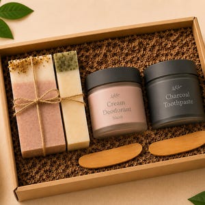 Può includere: Una confezione regalo contenente due saponette rettangolari legate con spago, un vasetto con etichetta Cream Deodorant blush, un vasetto con etichetta Charcoal Toothpaste e due piccole spatole di legno su un riempitivo di carta a nido d'ape.