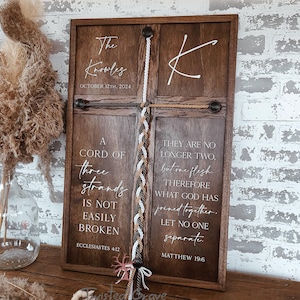 May include: A dark wood sign with white lettering and a braided rope design. The sign includes the text "The Knowles, October 12th, 2024" and Bible verses. A decorative piece for weddings or home decor.