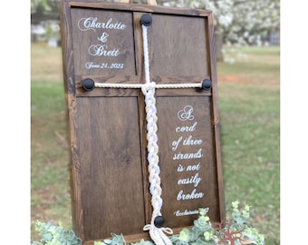 May include: A wooden sign with a white rope braid and the text "Charlotte & Brett June 24, 2023" and "A cord of three strands is not easily broken Ecclesiastes 4:12".