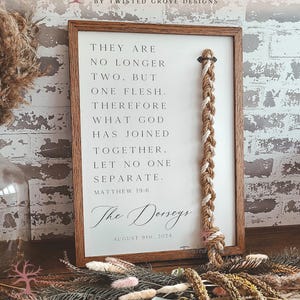 May include: A framed sign with a quote from Matthew 19:6, featuring a braided rope accent. The sign includes the names "The Dorseys" and the date August 9th, 2024. The frame is brown, and the background is white.
