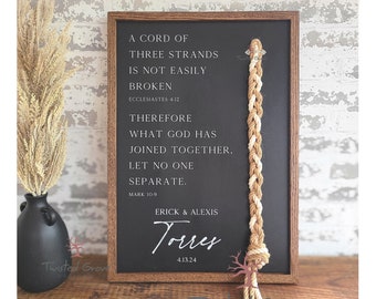 May include: A wooden sign with a black chalkboard insert featuring a trinity knot made of rope. The sign has the text "A cord of three strands is not easily broken. Ecclesiastes 4:12. Therefore what God has joined together, let no one separate. Mark 10:9. Erick & Alexis Torres 4.13.24"