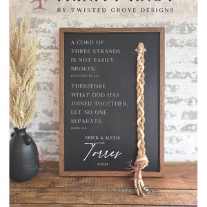 May include: A wooden sign with a black chalkboard insert featuring a trinity knot made of rope. The sign has the text "A cord of three strands is not easily broken. Ecclesiastes 4:12. Therefore what God has joined together, let no one separate. Mark 10:9. Erick & Alexis Torres 4.13.24"