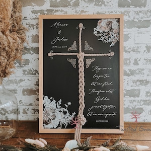 May include: A framed chalkboard sign with a rope cross design. The sign includes the names "Monica & Joshua" and the date "June 22, 2024". Floral accents and a Bible verse are also featured.