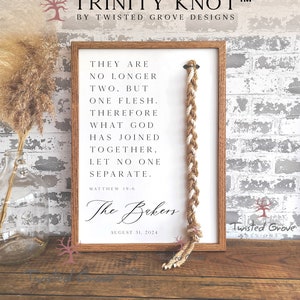 May include: A framed print with a white background and a brown wooden frame. The print features a braided rope knot with the text "They are no longer two, but one flesh. Therefore what God has joined together, let no one separate."  Matthew 19:6. The text "The Bakers" and "August 31, 2024" are also included. The print is a Trinity Knot, a symbol of love, faith, and hope.
