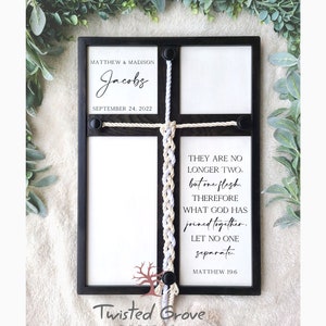 May include: A black wooden frame with a white background and a white and beige braided rope. The frame has a sign that says "Matthew & Madison Jacobs September 24, 2022". The frame also has a sign that says "They are no longer two, but one flesh. Therefore what God has joined together, let no one separate. Matthew 19:6".
