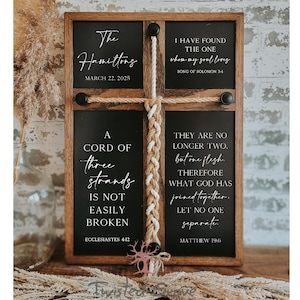 May include: A wooden sign with a braided rope in the center. The sign is divided into four sections with text on each section. The text includes the words "The Hamiltons", "A Cord of Three Strands", "I Have Found The One Whom My Soul Loves", and "They Are No Longer Two, But One Flesh".