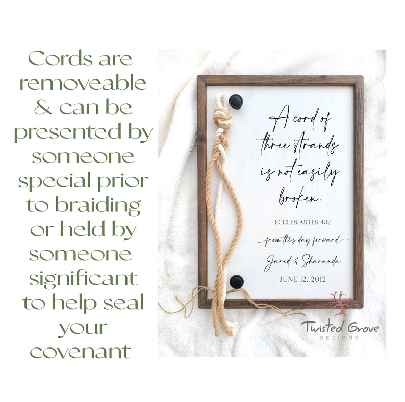 May include: A wooden sign with a white background and a brown frame. The sign features a quote from Ecclesiastes 4:12, "A cord of three strands is not easily broken." The quote is written in black cursive font. Below the quote, the text "from this day forward" is written in a smaller font. The names "Jared & Sharanda" are written below that, followed by the date "June 12, 2012". The sign is decorated with three cords, two brown and one white, that are tied together in a knot at the top. The cords are hanging down the sides of the sign. The sign is also decorated with a black metal button.