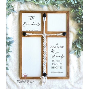May include: Wooden framed wall art with a cross design. The art piece features the text "The Barnharts JULY 23, 2022" and "A CORD OF three strands IS NOT EASILY BROKEN ECCLESIASTES 4:12". The cross is made of woven rope and black buttons.