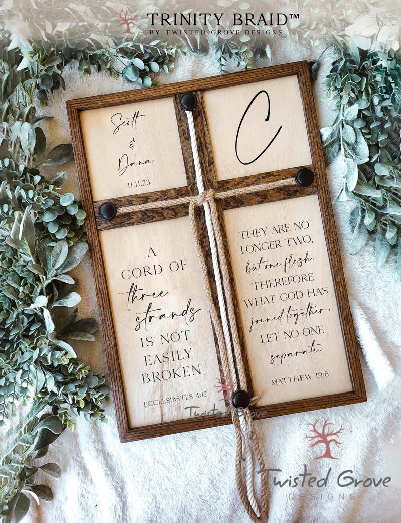 May include: A wooden sign with a rope braid in the center. The sign has the text "A cord of three strands is not easily broken" and "Ecclesiastes 4:12" on the left side. The right side has the text "They are no longer two, but one flesh. Therefore what God has joined together, let no one separate." and "Matthew 19:6". The sign also has the names "Scott & Dana" and the date "11.11.23" on the top left side.