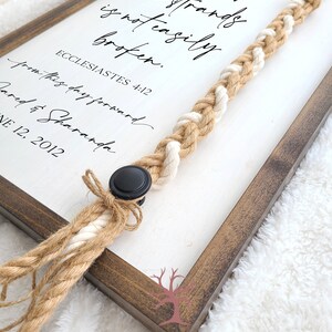 May include: A framed sign with the text "A cord of three strands is not easily broken. Ecclesiastes 4:12" with a braided rope attached to the frame.
