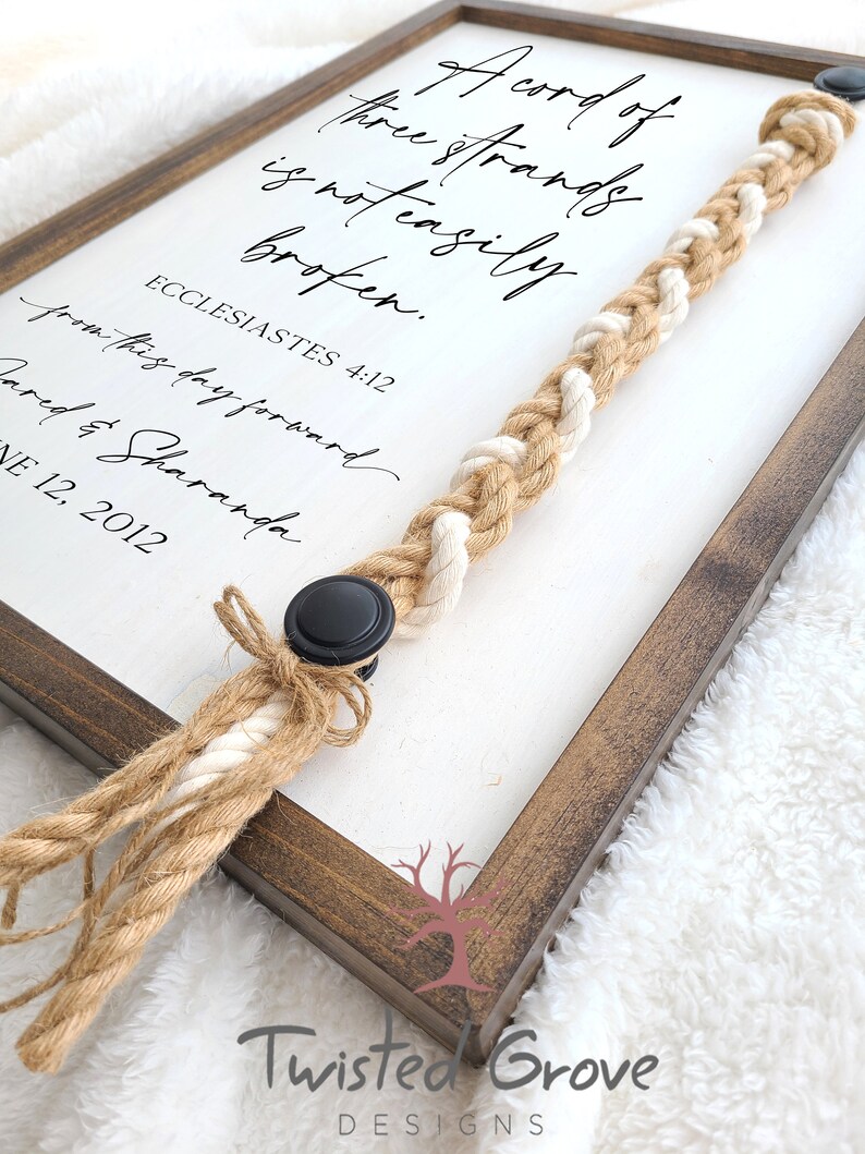 May include: A framed sign with the text "A cord of three strands is not easily broken. Ecclesiastes 4:12" with a braided rope attached to the frame.