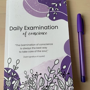 May include: A purple and white journal with the text "Daily Examination of conscience" and a quote from Saint Ignatius of Loyola. The journal has a floral design.