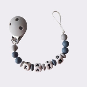 Op de afbeelding: Een grijze en blauwe siliconen baby-bijtje met een clip en kralen die de naam "KAIS" spellen.