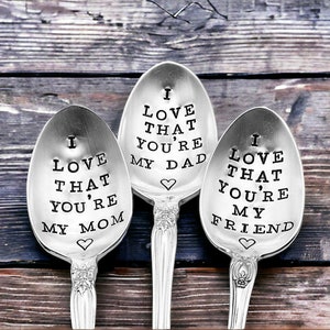 May include: Three silver spoons with stamped text. The spoons read "I love that you're my mom", "I love that you're my dad", and "I love that you're my friend". Each spoon has a decorative handle and a heart symbol.