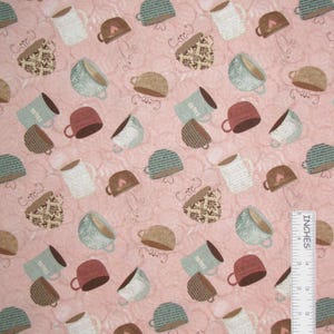 May include: A pink fabric featuring a repeating pattern of various coffee mugs in shades of brown, white, and teal, with some mugs displaying text or floral designs. A white L-shaped ruler is positioned in the corner for scale reference.