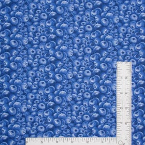 May include: A blue fabric featuring a dense, repeating pattern of blueberries. An L-shaped metal ruler is placed over the fabric, with the vertical arm measuring 6 inches and the horizontal arm measuring 6 inches, providing a scale for the print.