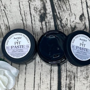 May include: Two black jars of natural pit paste deodorant, each labeled "Hard Velvet Pit Paste All Natural Armpit Detox" with a white label and black text. The jars are on a light brown textured surface.