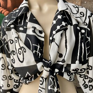 May include: A black and white patterned blouse with a tie front. The blouse is made of a sheer fabric and has long sleeves.
