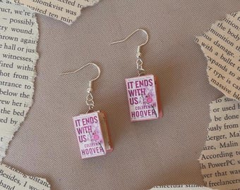 May include: Silver-tone dangle earrings featuring miniature book charms. Each charm displays the book title "IT ENDS WITH US" by Colleen Hoover on a pink cover. A unique accessory for book lovers.