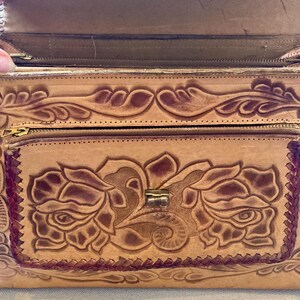 Pode incluir: Uma bolsa de couro castanho claro com um design floral. A bolsa apresenta um padr&atilde;o de rosas em relevo na frente, um bolso com z&iacute;per e um fecho de metal. As bordas s&atilde;o costuradas com linha castanha mais escura.