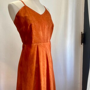 May include: A long, sleeveless, orange dress with a V-neckline. The dress is made of a soft, flowing fabric.