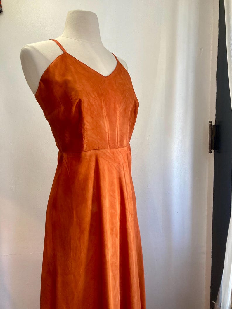 May include: A long, sleeveless, orange dress with a V-neckline. The dress is made of a soft, flowing fabric.