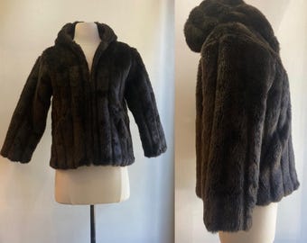 May include: A dark brown faux fur jacket with a zip-up front and a hood. The jacket is displayed on a mannequin, showcasing its texture and design. The jacket's fur appears soft and plush, offering a warm and stylish look.