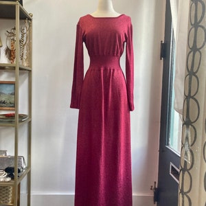 May include: A long, burgundy knit dress with a fitted bodice and a flowing skirt. The dress has a subtle shimmer and a slightly stretchy fabric.