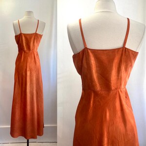 May include: A long, burnt orange, sleeveless maxi dress with a simple, straight cut and a V-neckline.