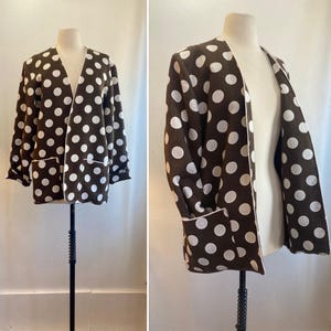 May include: A brown and white polka dot cardigan with a long sleeve and a shawl collar. The cardigan is open in the front and has a white trim around the edges.