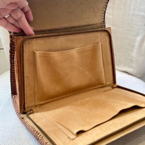 Pode incluir: Vista aberta de uma pasta de couro castanho claro vintage. A pasta tem fecho de correr, v&aacute;rios bolsos interiores e uma borda costurada decorativa. O interior &eacute; um tom mais claro do que o exterior.