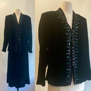 May include: A black velvet two-piece suit. The jacket and skirt are displayed on a mannequin. The jacket has a V-neck and is embellished with sequins and beads. The skirt is a midi length.