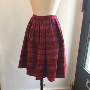 May include: A red, pink, and black patterned skirt with a pleated waistline. The skirt is knee-length and has a flared silhouette.