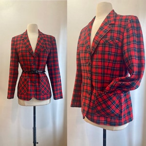 May include: A red and black plaid blazer with a V-neck, long sleeves, and a black belt. The blazer has a classic design with a pocket on the front. The jacket is displayed on a mannequin.