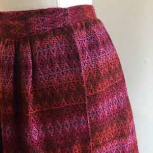 May include: A red, pink, and black skirt with a chevron pattern. The skirt is made of a woven fabric and has a pleated design.