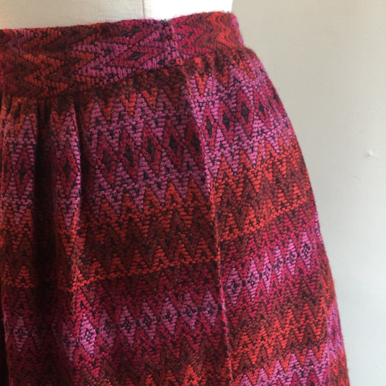 May include: A red, pink, and black skirt with a chevron pattern. The skirt is made of a woven fabric and has a pleated design.