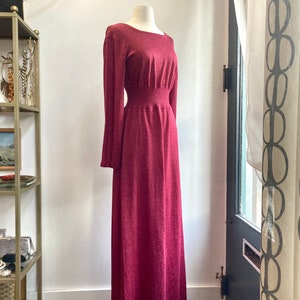 May include: A long-sleeved, burgundy maxi dress with a fitted bodice and a flowing skirt. The dress has a subtle shimmer and a cinched waist.