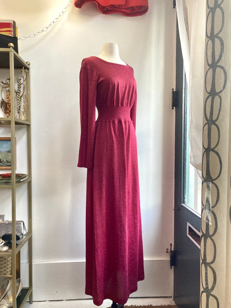 May include: A long-sleeved, burgundy maxi dress with a fitted bodice and a flowing skirt. The dress has a subtle shimmer and a cinched waist.