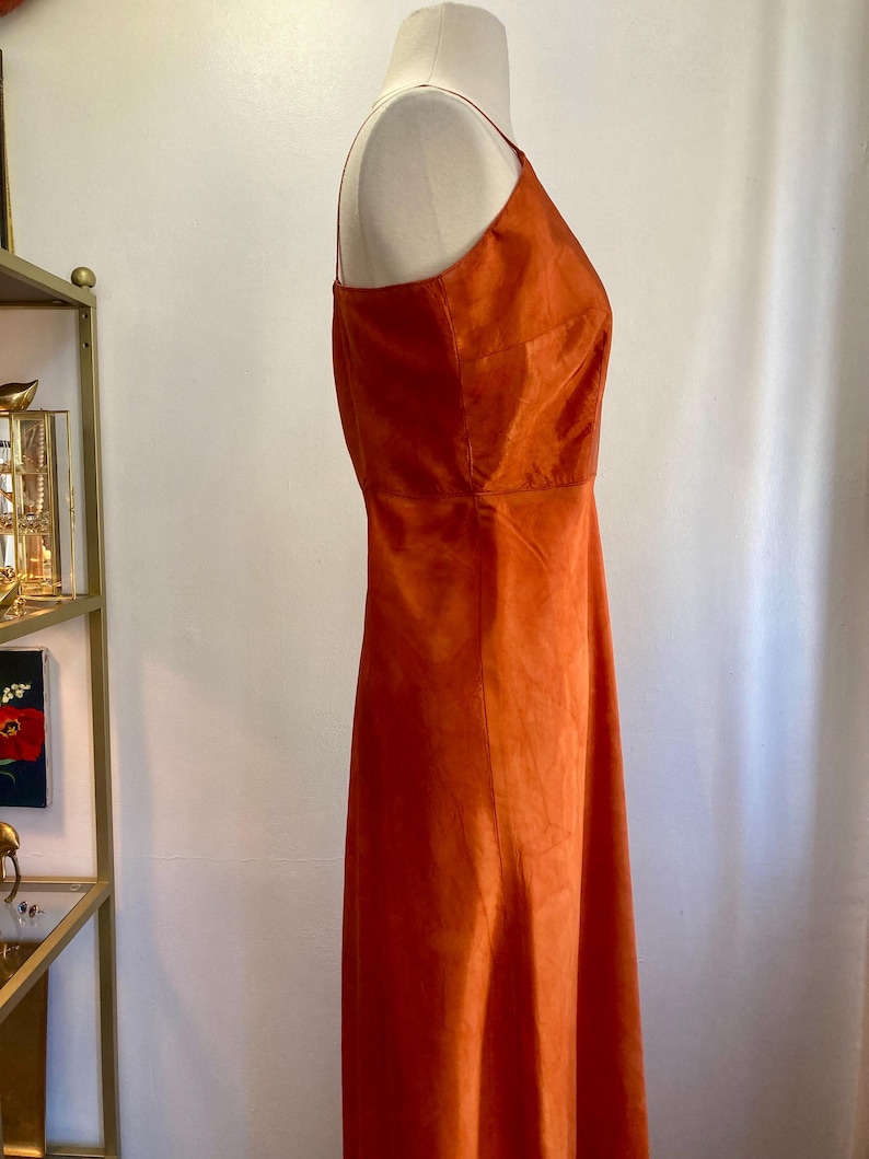May include: A burnt orange sleeveless maxi dress with a halter neckline. The dress is made of a soft, flowing fabric.