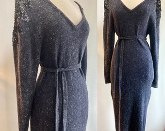 May include: A long-sleeved, dark gray sweater dress with a V-neckline and a tie belt. The dress has sequined embellishments on the shoulders.