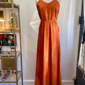 May include: A long, burnt orange, sleeveless dress with a V-neckline. The dress is made of a soft, suede-like material.