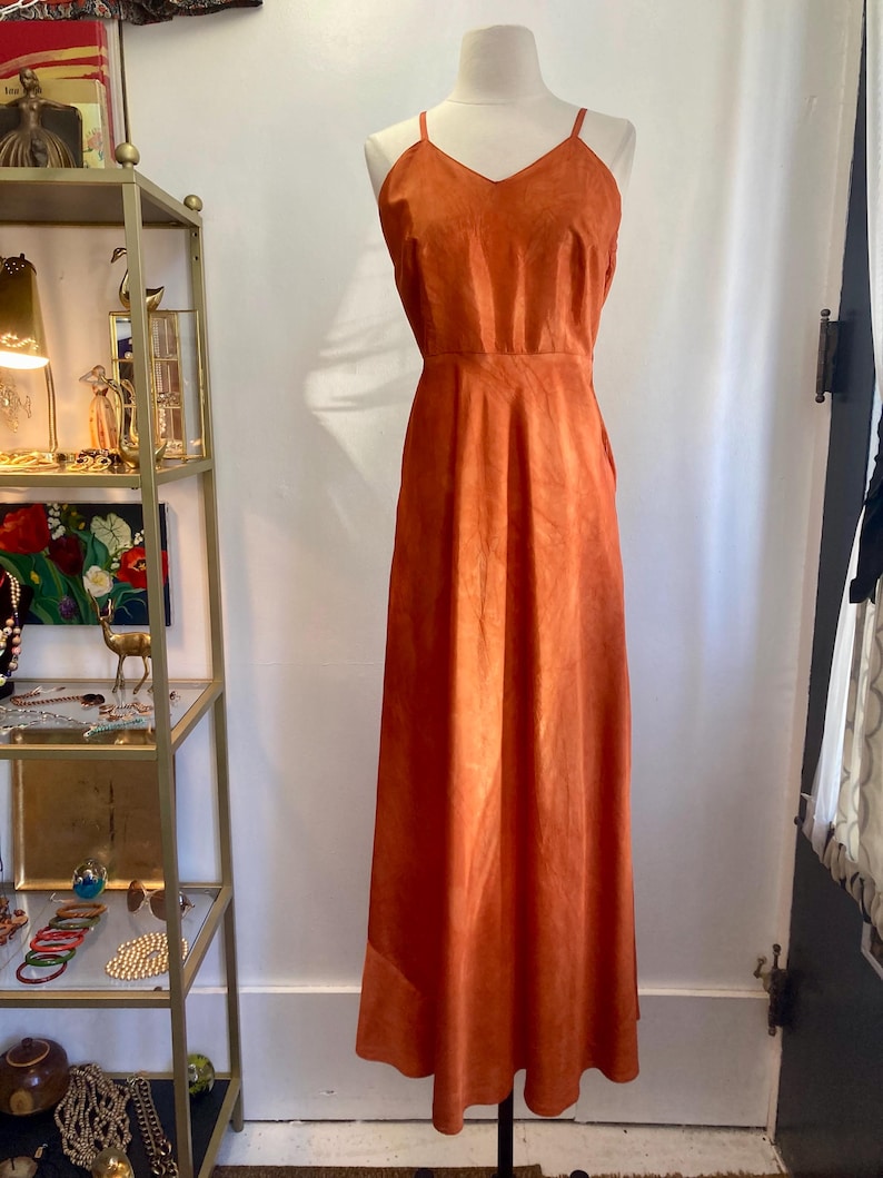 May include: A long, burnt orange, sleeveless dress with a V-neckline. The dress is made of a soft, suede-like material.