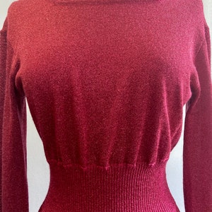 May include: A long-sleeved, burgundy knit dress with a fitted bodice and a flowing skirt. The dress has a subtle shimmer and a ribbed texture.