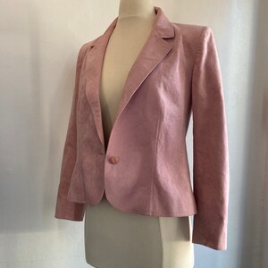 May include: A pink suede blazer with a single button closure. The blazer has a classic, tailored fit and long sleeves.