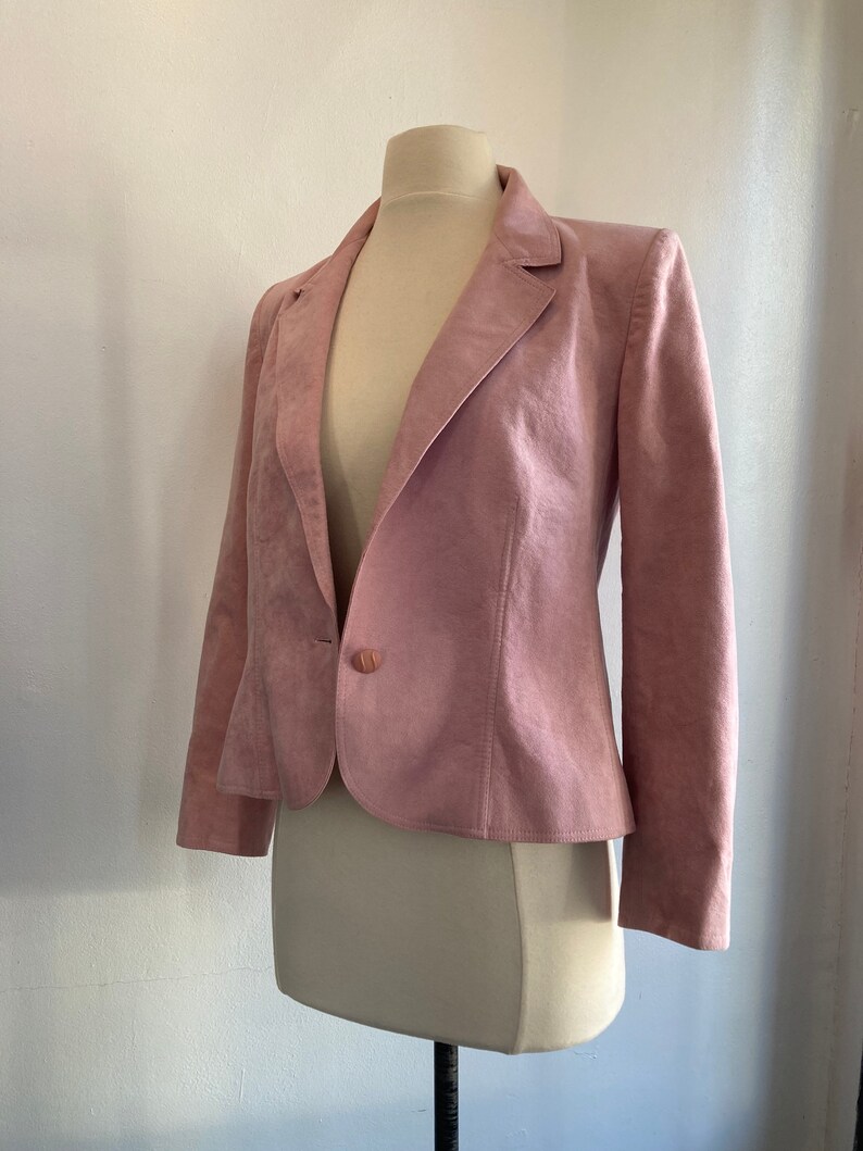 May include: A pink suede blazer with a single button closure. The blazer has a classic, tailored fit and long sleeves.