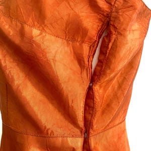 May include: A close-up of the back of an orange dress with a zipper closure. The dress is made of a shiny, silky fabric.