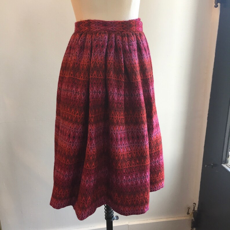 May include: A pleated midi skirt with a geometric pattern in shades of pink, orange, and brown.