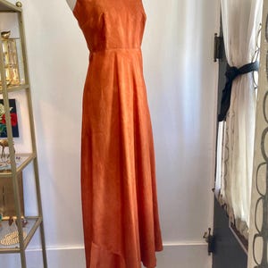 May include: A long, burnt orange, sleeveless maxi dress with a V-neckline.