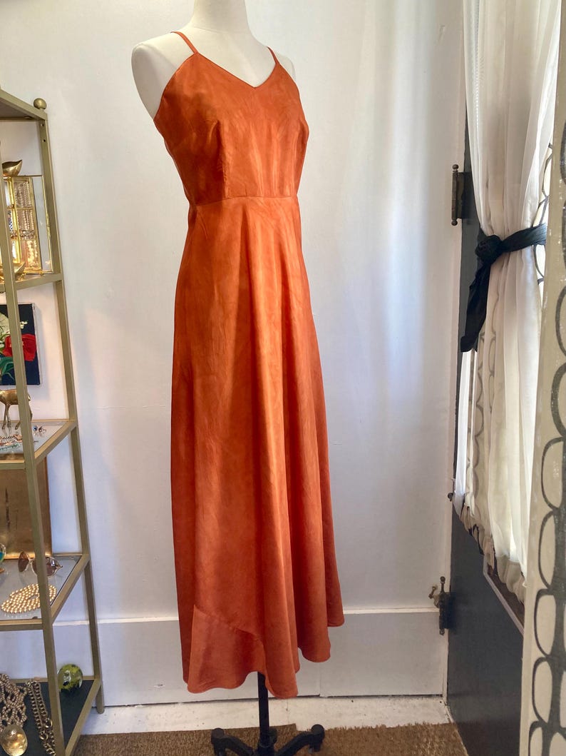 May include: A long, burnt orange, sleeveless maxi dress with a V-neckline.