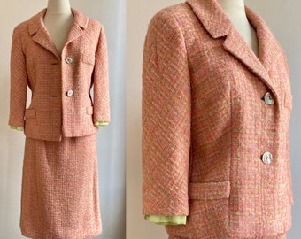 May include: A pink and green tweed skirt suit with a jacket and a skirt. The jacket has a notched collar, two pockets, and three buttons. The skirt is knee-length and has a straight silhouette.